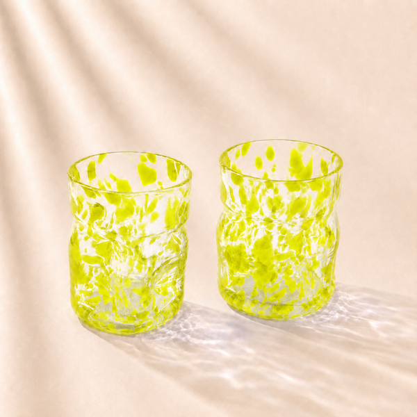 Two green glass tumblers on a beige fabric background