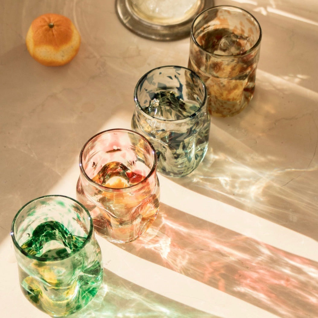 Set of colorful glass tumblers on a reflective surface with an orange fruit. - lifestyle