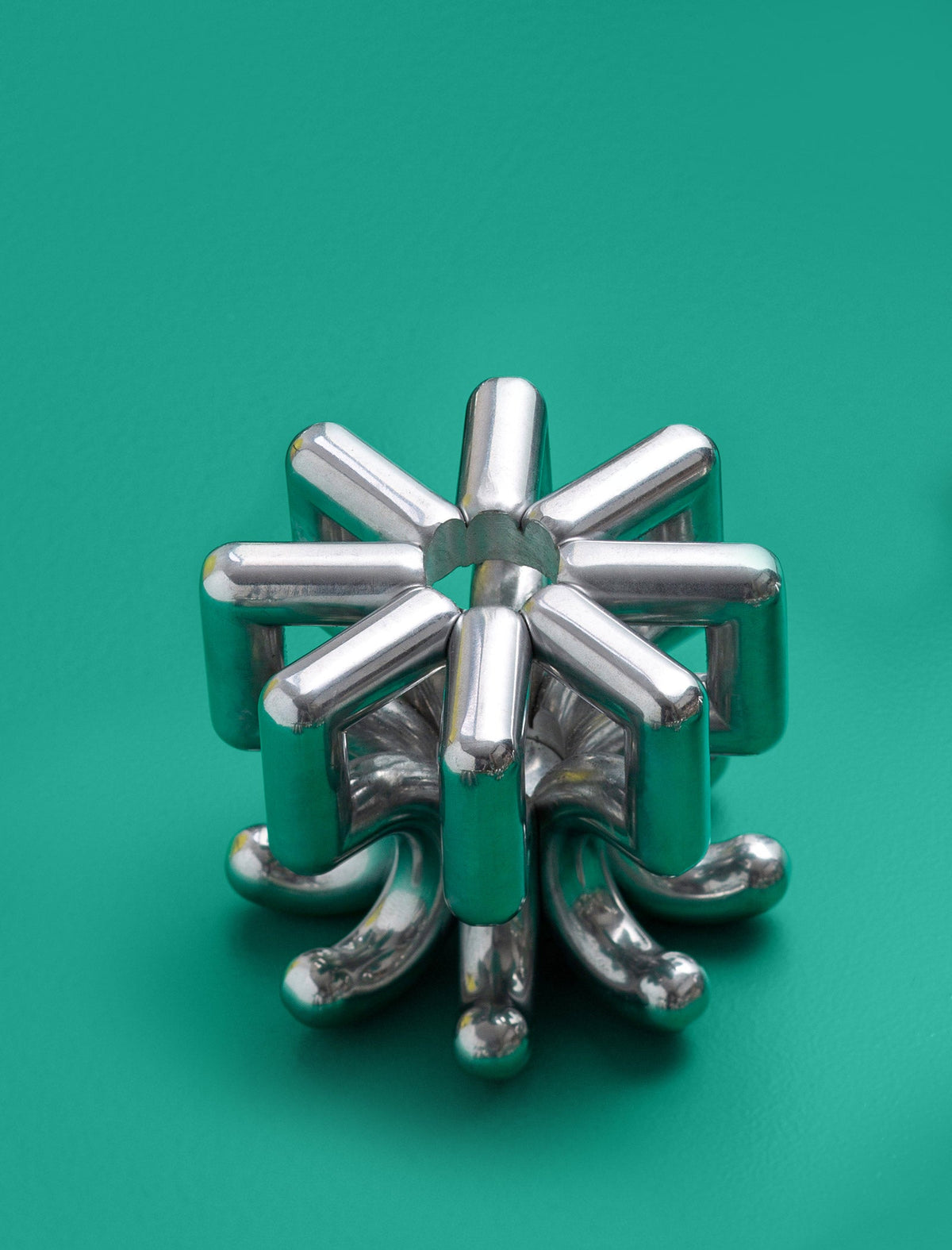 DIGIT FIVE Candlestick made of polished solid aluminum with a modern geometric design on a green background.
