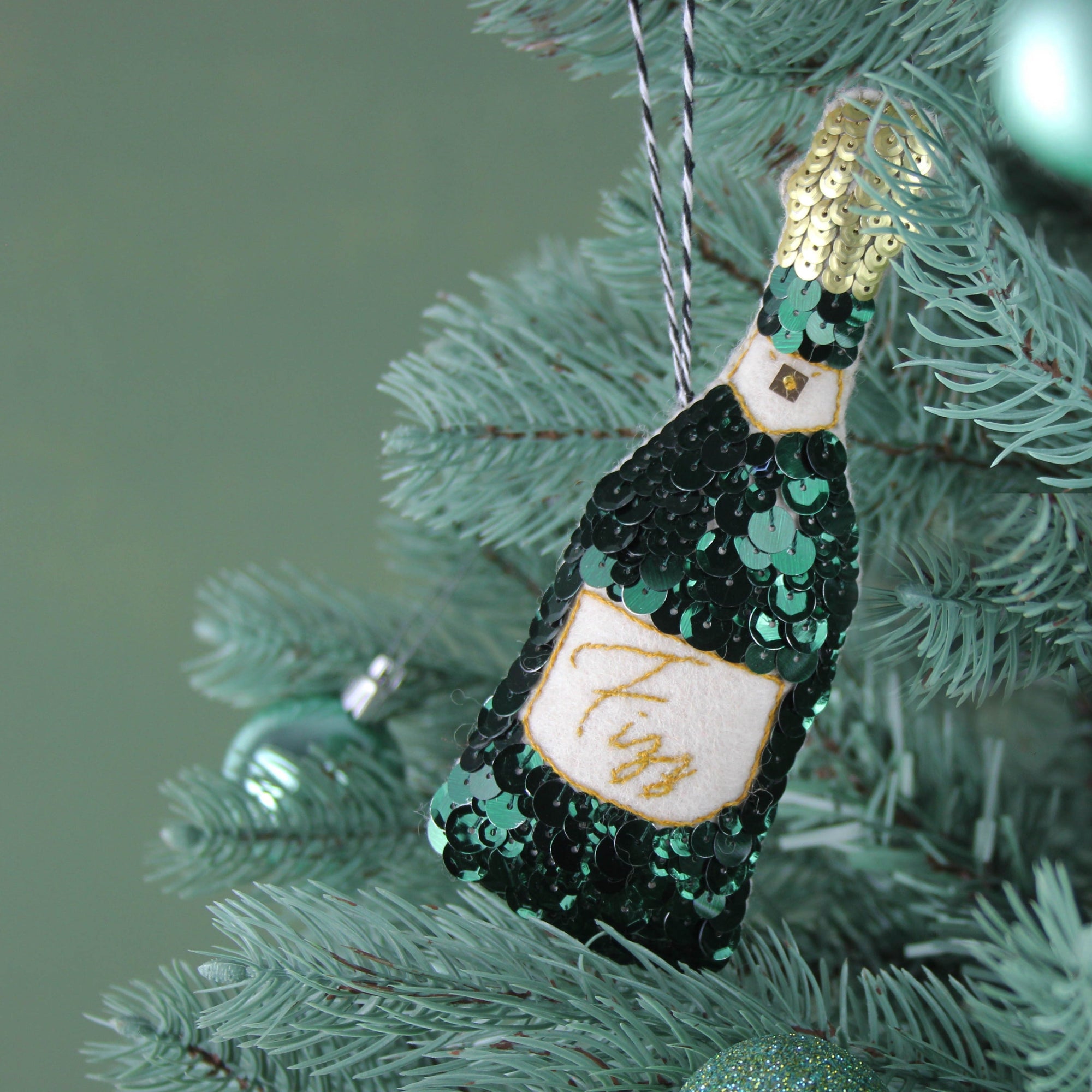 A green sequinned champagne bottle ornament on a green tree