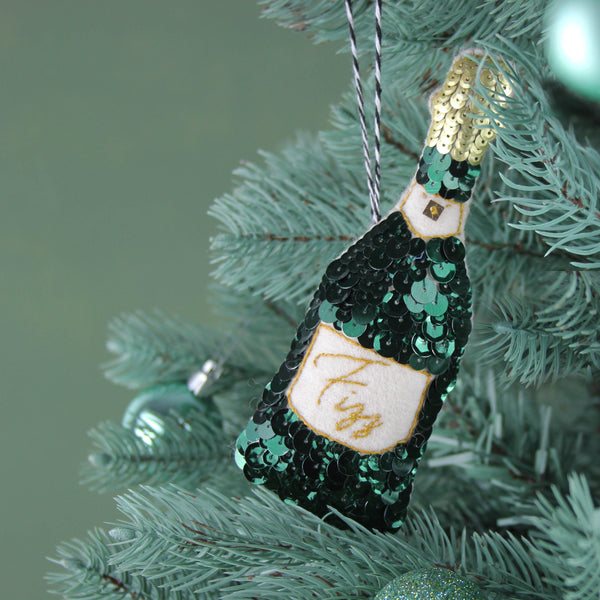 A green sequinned champagne bottle ornament on a green tree