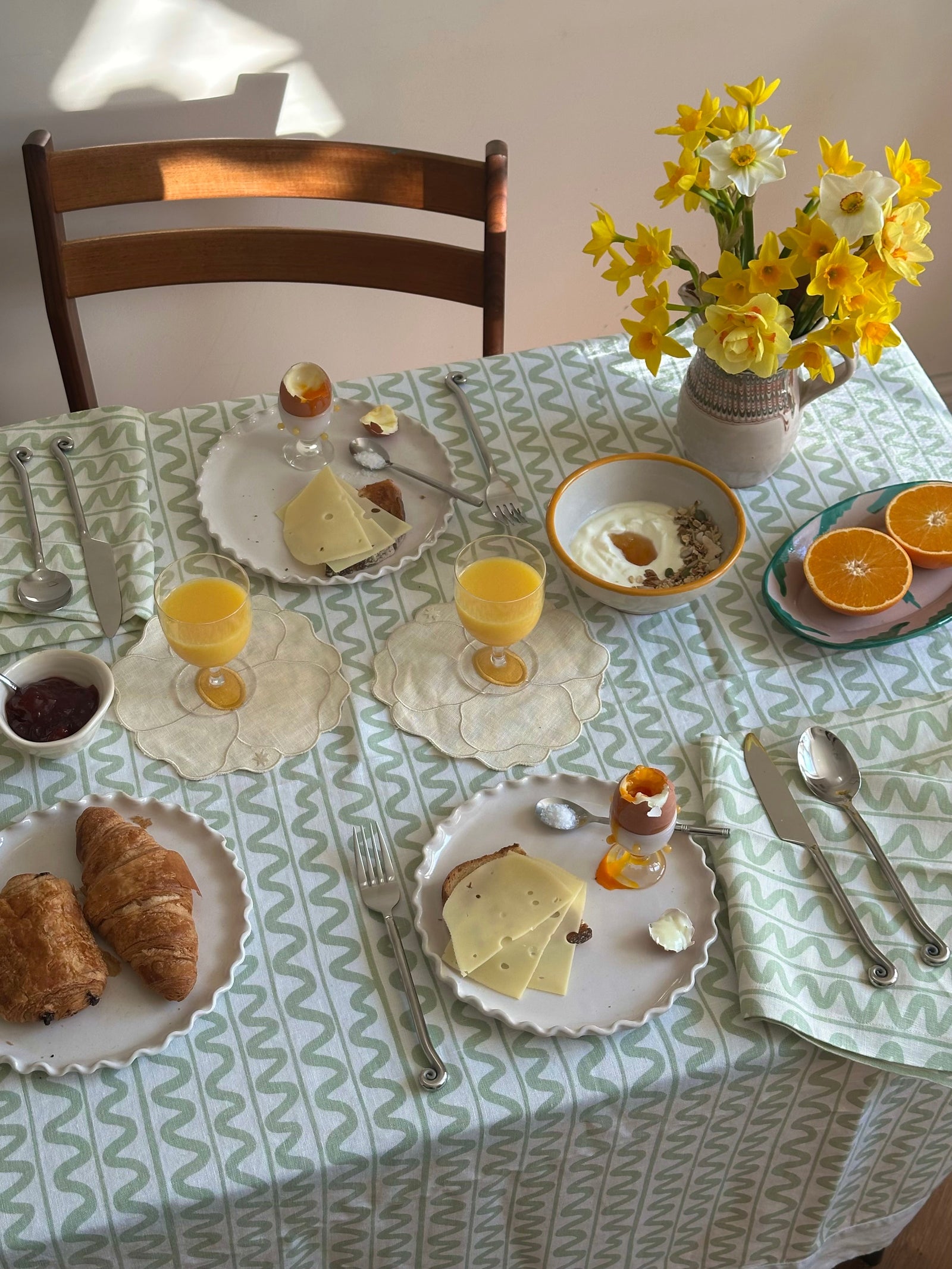 Dining table set for breakfast with croissants, eggs, and a vase of flowers.