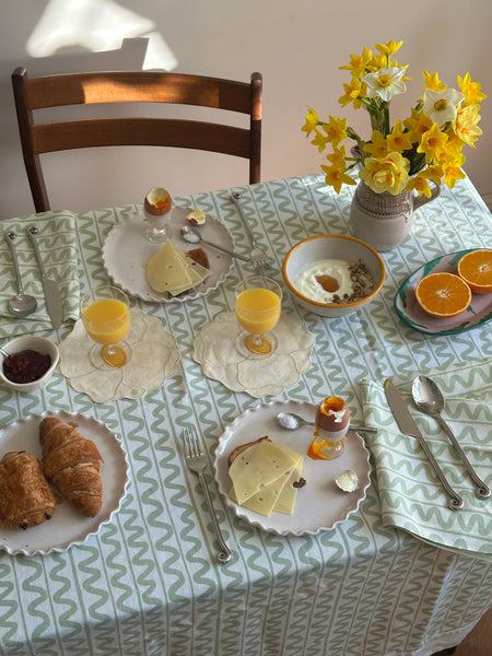 Dining table set for breakfast with croissants, eggs, and a vase of flowers.