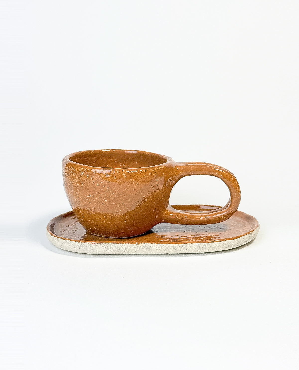 A brown ceramic mug with a caramel glaze and an oval plate, on a white background.