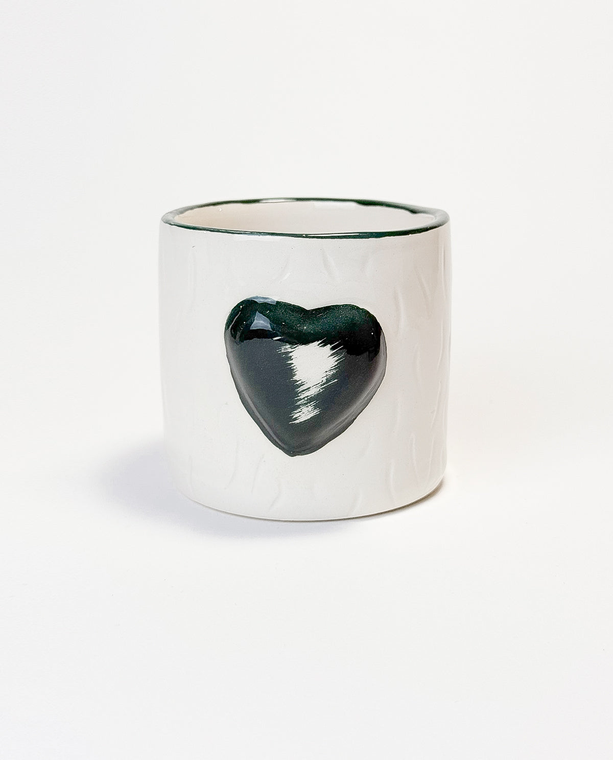 A white ceramic mug with a embossed green heart on the side.