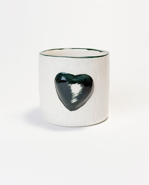 A white ceramic mug with a embossed green heart on the side.