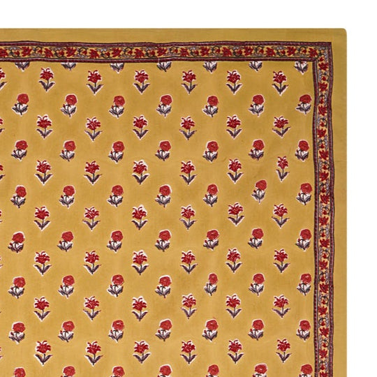 A rectangular tablecloth with a golden yellow base and small floral motifs, with a decorative border.