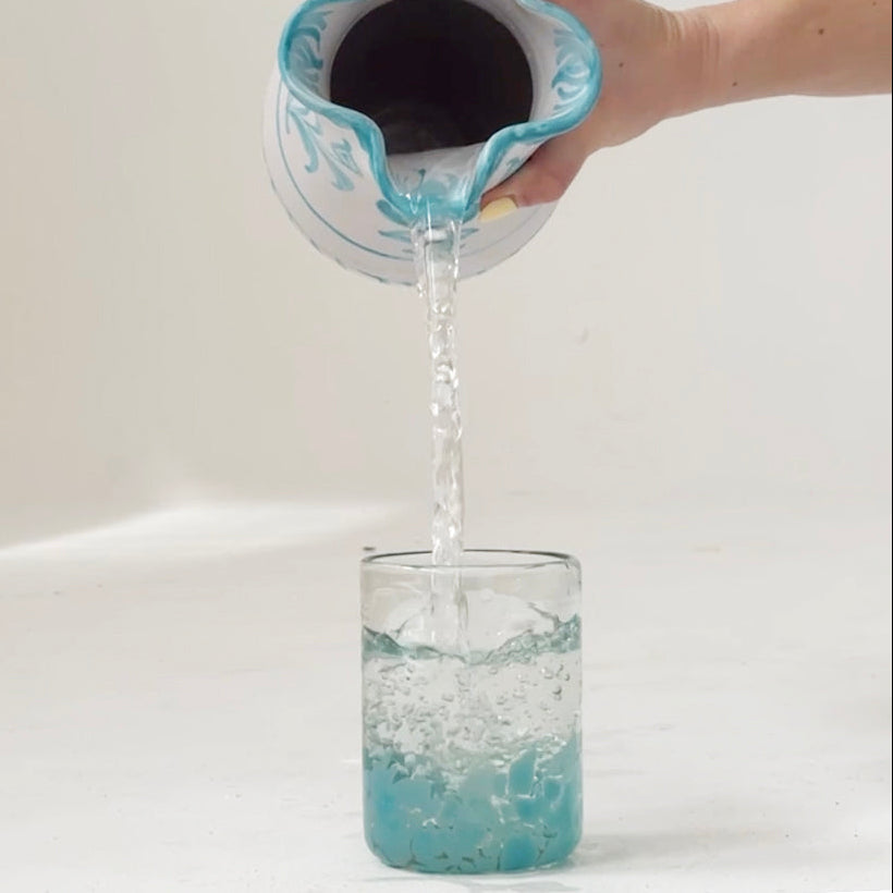 Person pouring blue liquid from a container into a glass on a white background - lifestyle