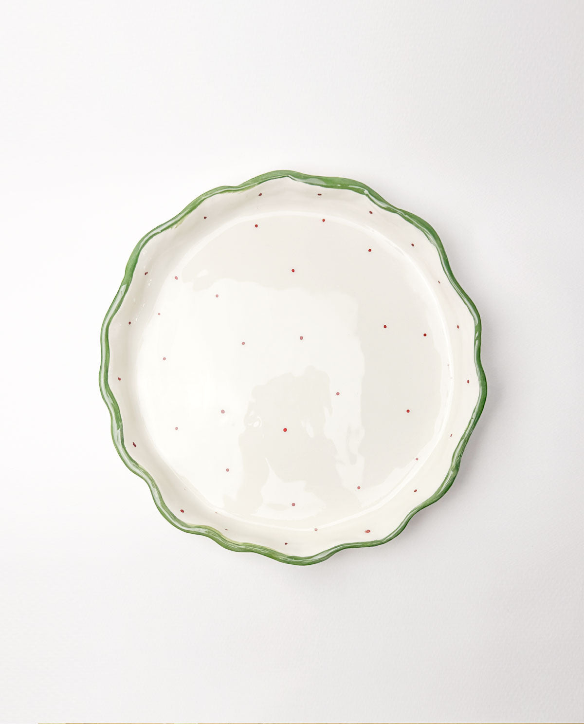 White festive ceramic plate with green rim and red speckles on a white background
