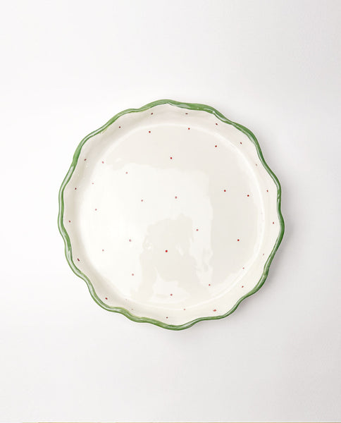 White festive ceramic plate with green rim and red speckles on a white background