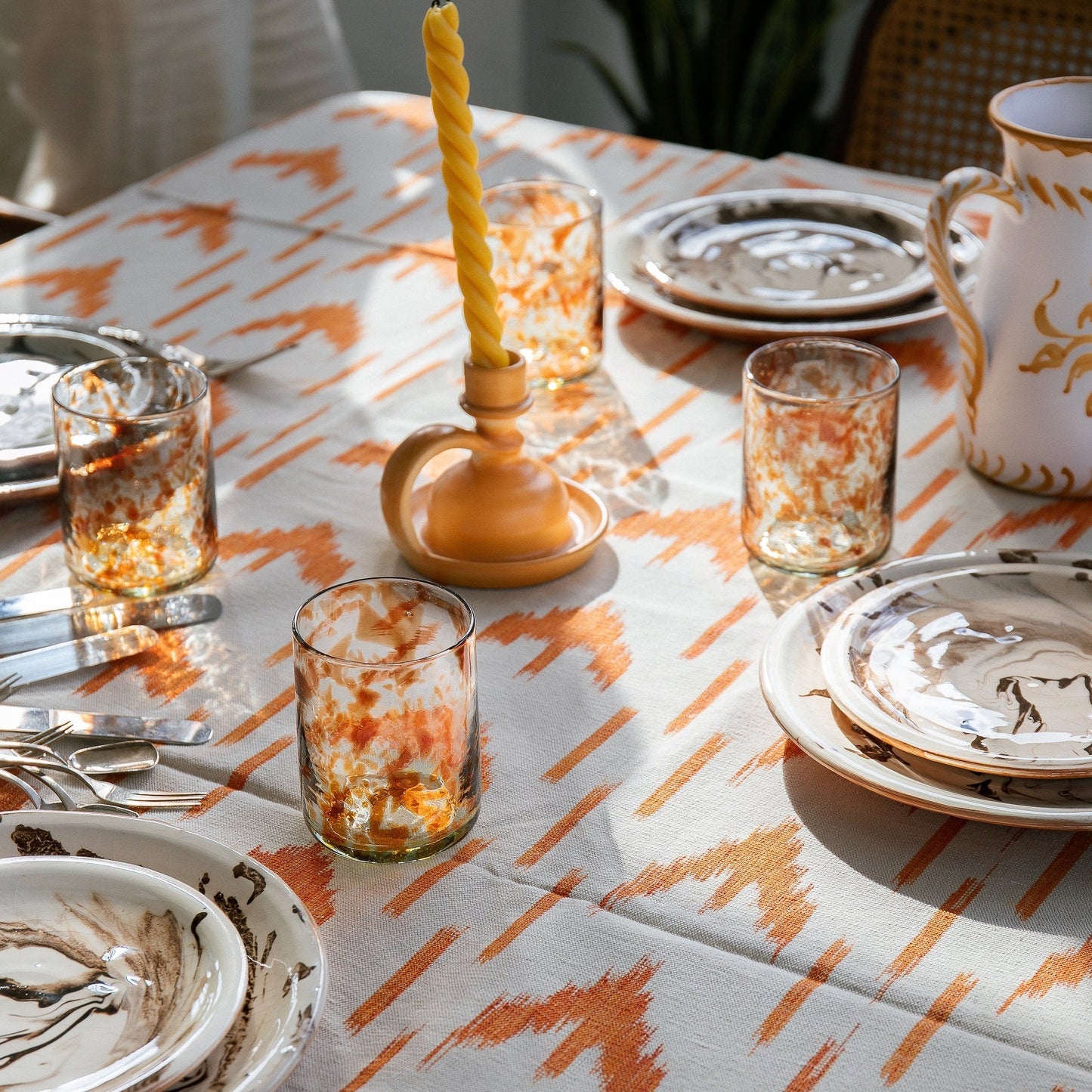 Dining table setting with patterned tablecloth, glasses, and ceramic items. - lifestyle
