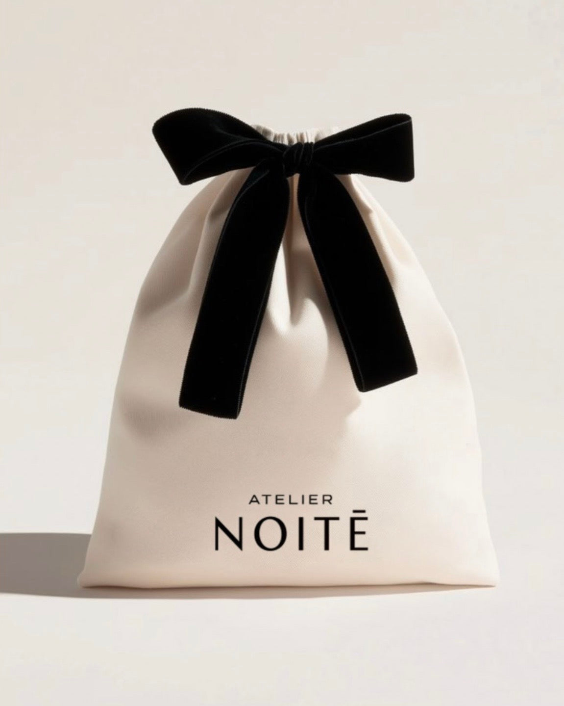 Beige drawstring bag with black velvet ribbon and 'Atelier Noite' branding on a light background