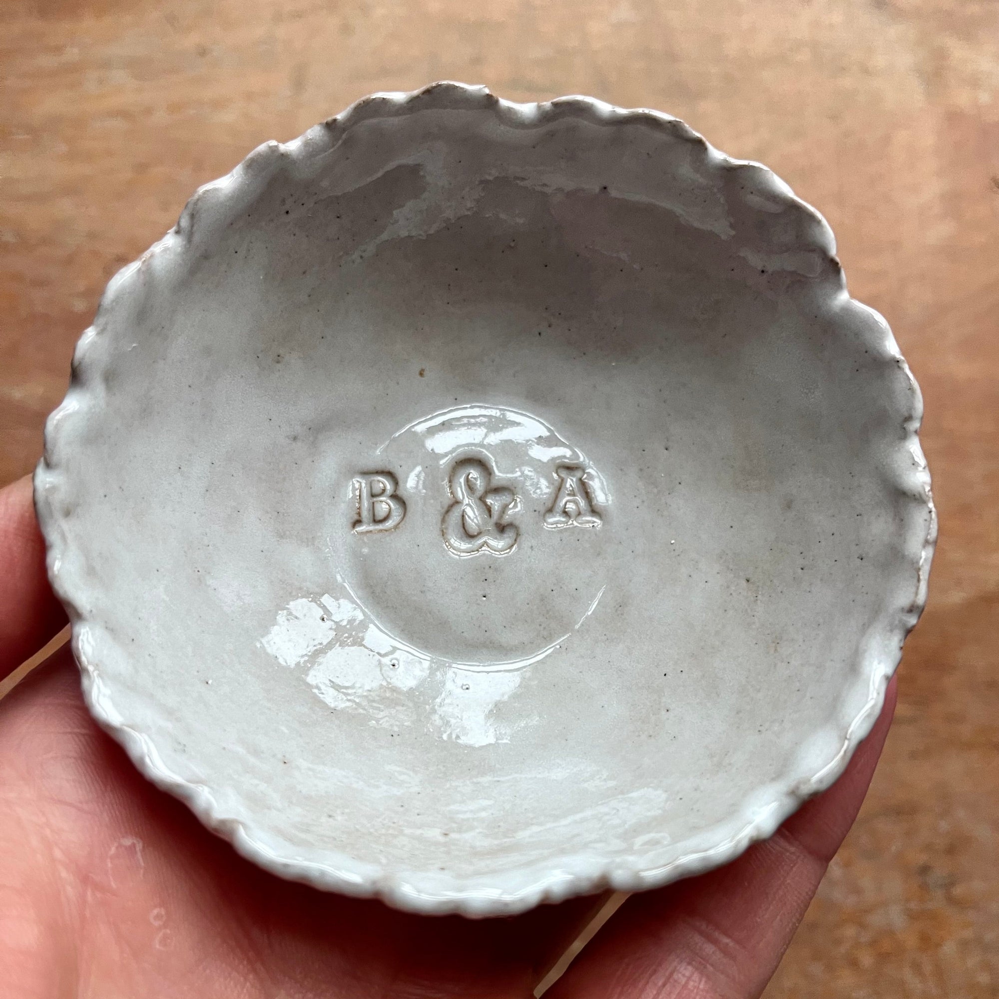 White ceramic bowl with 'B & A' branding held in a hand on a wooden surface