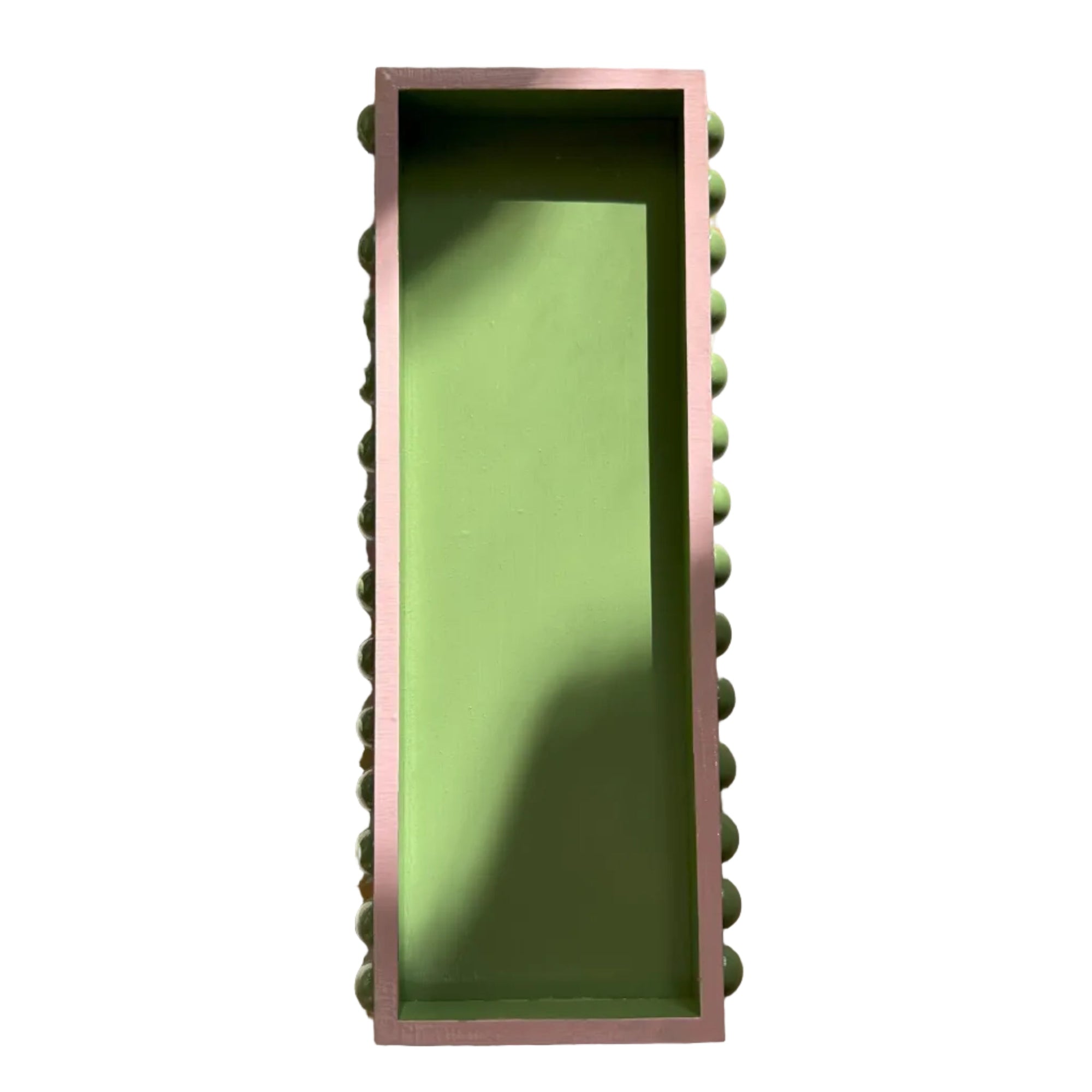 A hand painted decorative wooden tray with a green bobbin style design and pink edges, displayed on a patterned background.