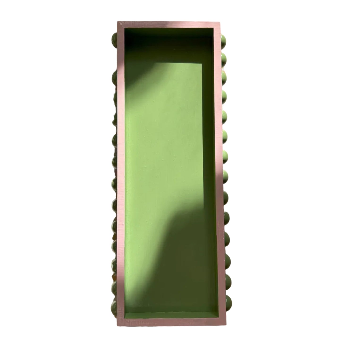 A hand painted decorative wooden tray with a green bobbin style design and pink edges, displayed on a patterned background.