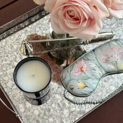 Decorative tray with pink roses, a candle, and a green silk mask on a reflective surface.