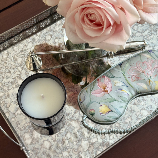 Decorative tray with pink roses, a candle, and a green silk mask on a reflective surface.