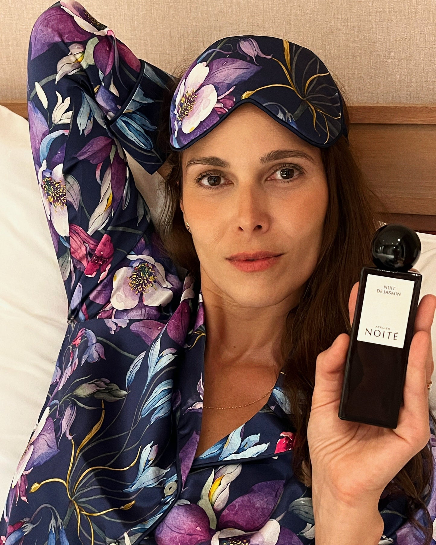 Woman in floral pajama set holding a black bottle labeled 'Noite' with a matching headband.