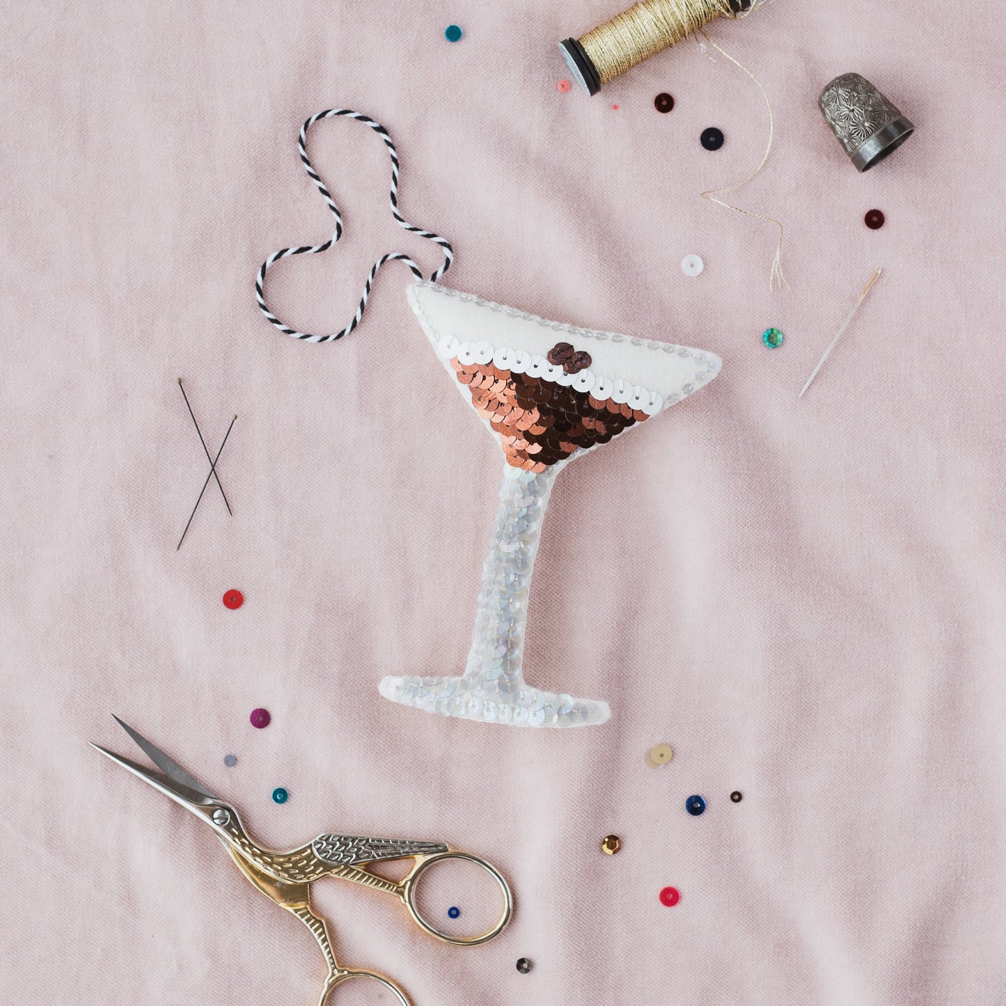 The Espresso Martini Sequin Ornament on a pink background with sequins scattered around