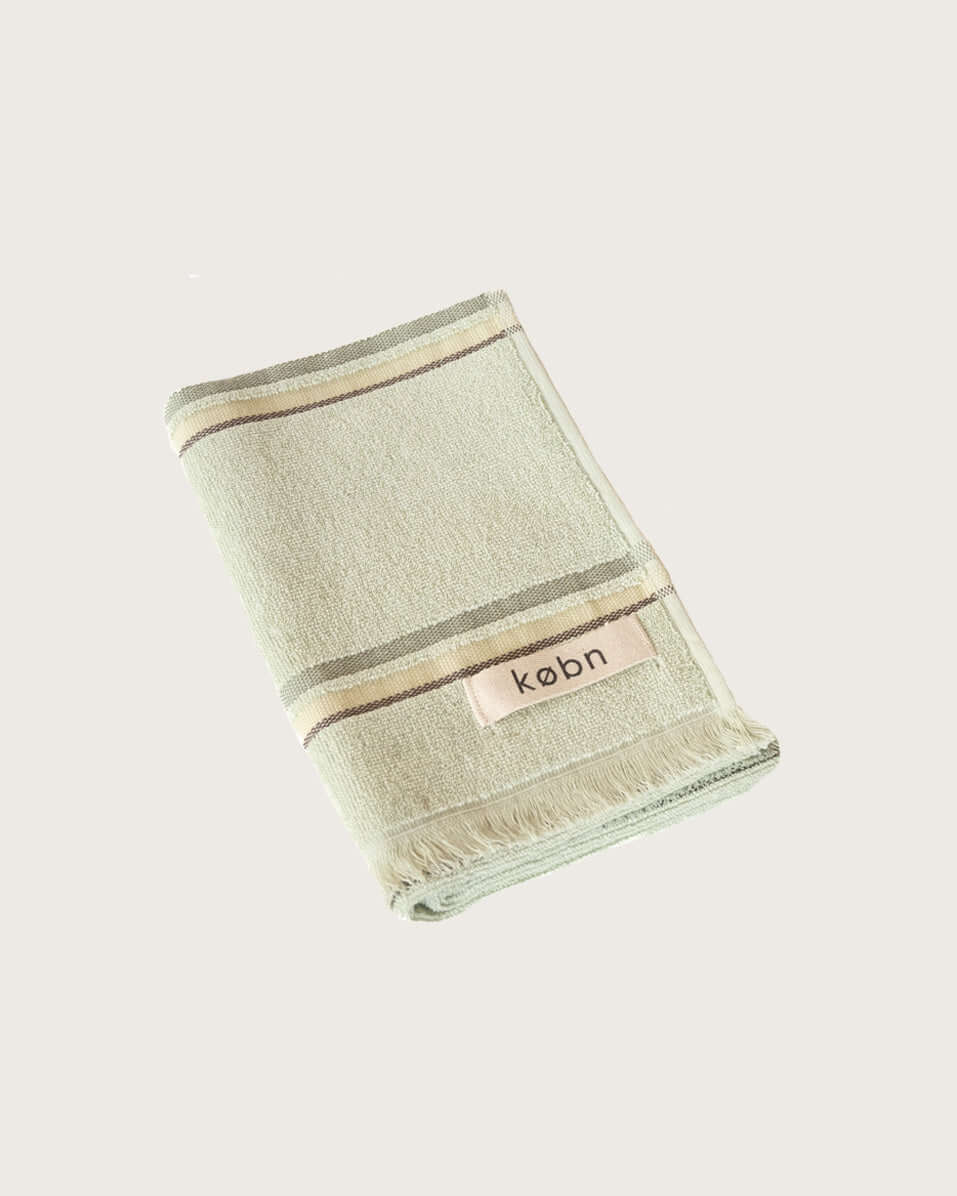 Folded mint hand  towel with stripes and 'kobn' branding on a light beige background