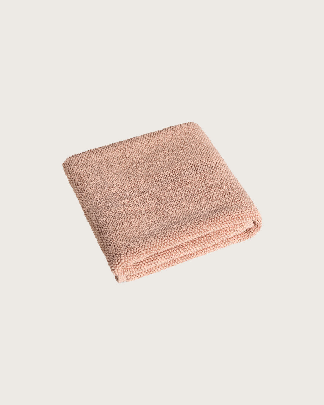 Folded pink bathmat on a light beige background