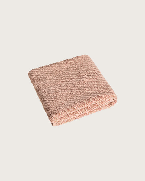 Folded pink bathmat on a light beige background