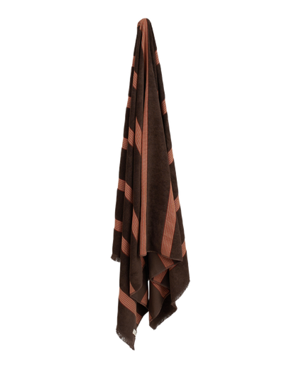 Dark brown towel with red stripes hanging on blank wall.