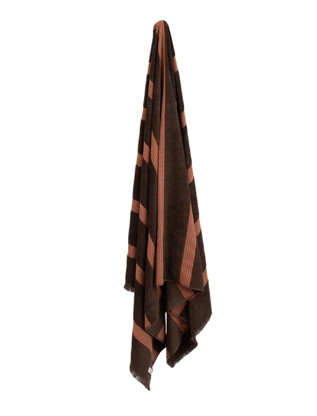 Dark brown towel with red stripes hanging on blank wall.