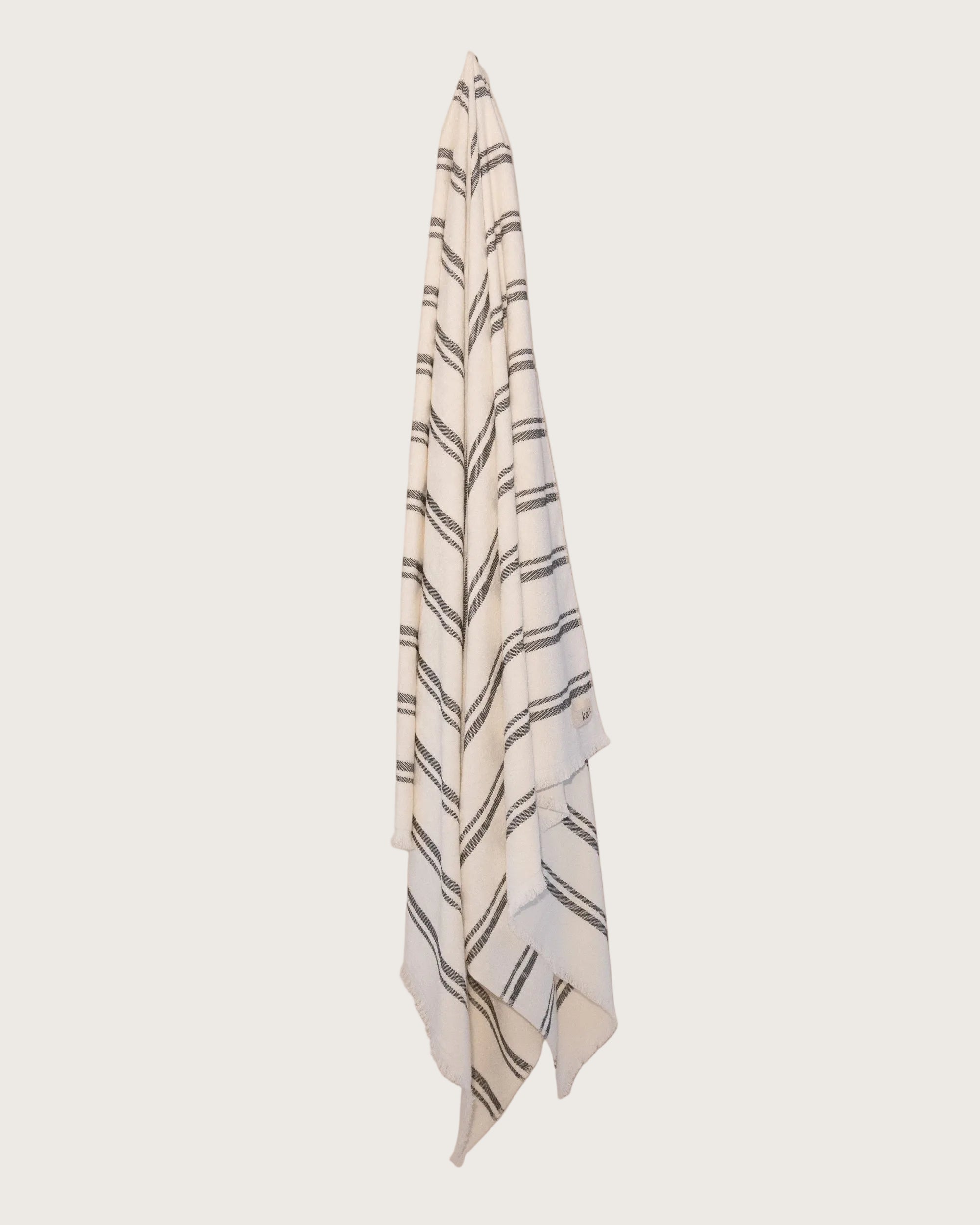Kobn Crema towel with black stripes hanging on a butter yellow background