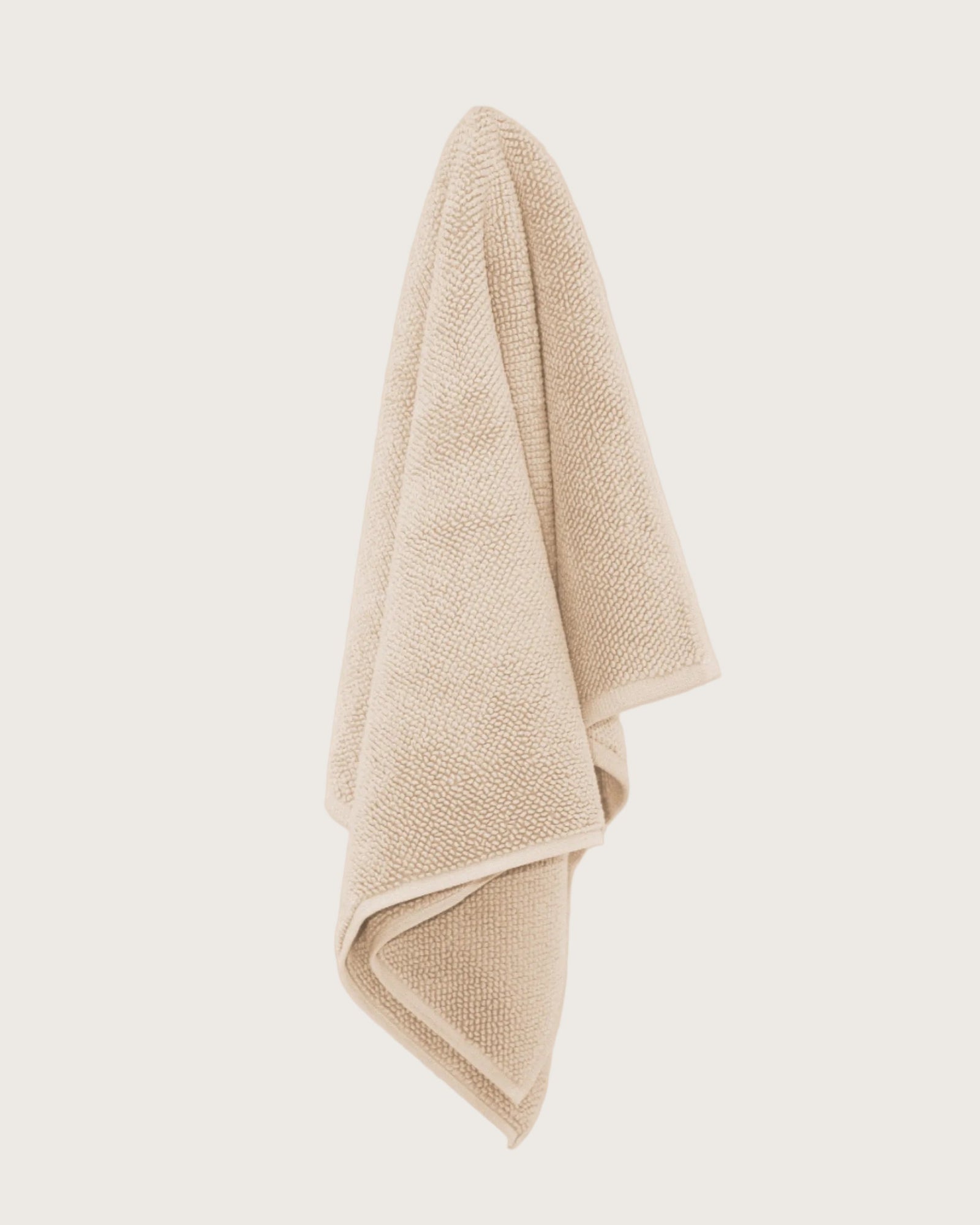 Chunky cotton textured bathmat in sand colour hanging against a neutral wall. 