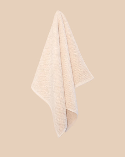 Chunky cotton weave bathmat in ecru colour hanging on a soft beige background. 