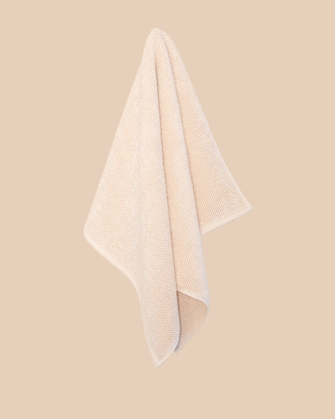 Chunky cotton weave bathmat in ecru colour hanging on a soft beige background. 