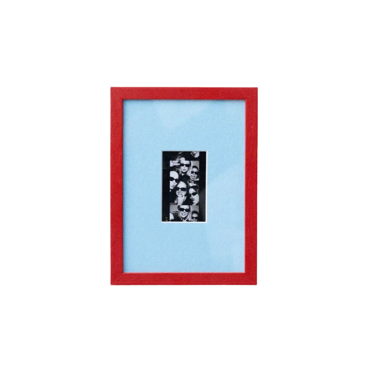 A framed art print featuring a black and white collage in a vertical black frame, set against a light blue mat and a vibrant red outer frame, mounted on a plain white wall.