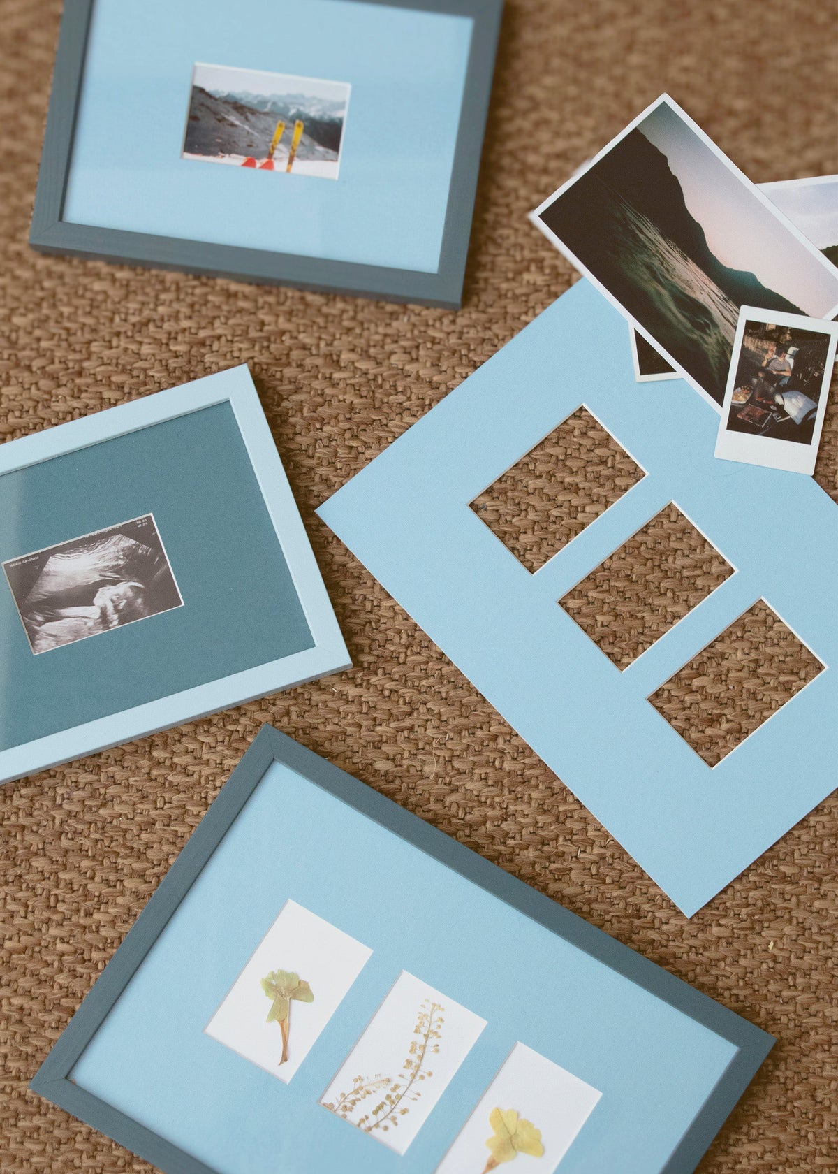 A styled flat-lay of light blue picture frames and matching mat boards arranged on a brown woven rug, with a few sample photographs placed on top.