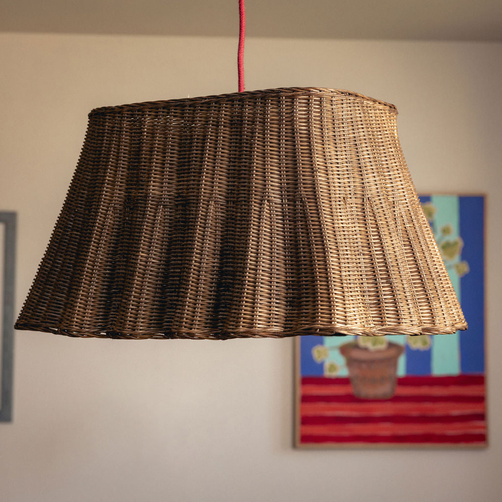 Wicker lampshade hanging against a wall with a colorful painting in the background