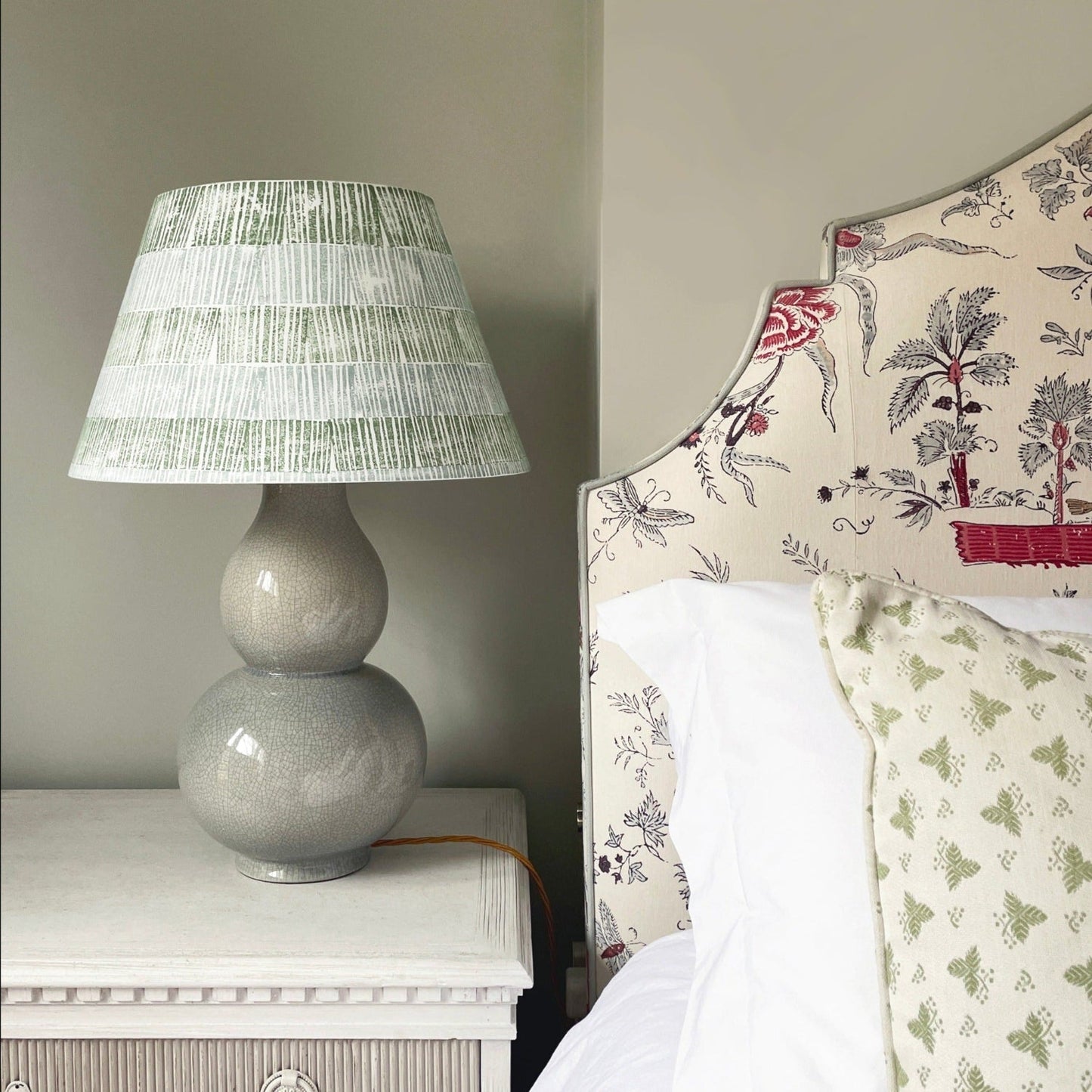 Empire lampshade with green and blue stripes, bold stripe design paired with a ceramic double-gourd lamp base beside a patterned upholstered headboard.