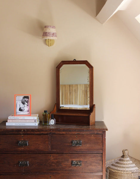 Burgundy and pink striped lampshade mounted on a brass wall fitting, bold lampshade styled above a vintage wooden chest of drawers with framed artwork and decorative accents.