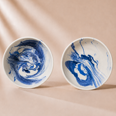 Two ceramic bowls with blue and white marbled design on a beige background