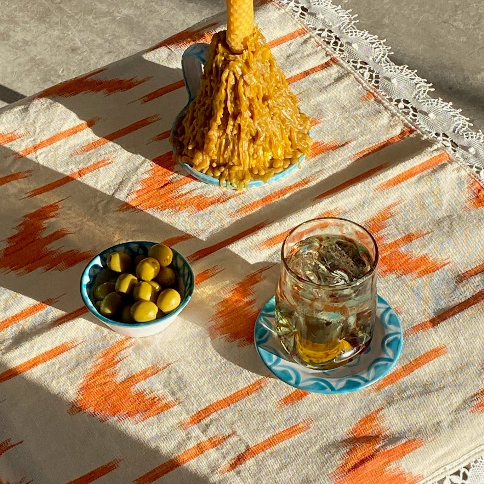 Candle, bowl of olives, and glass with ice on a patterned tablecloth - lifestyle