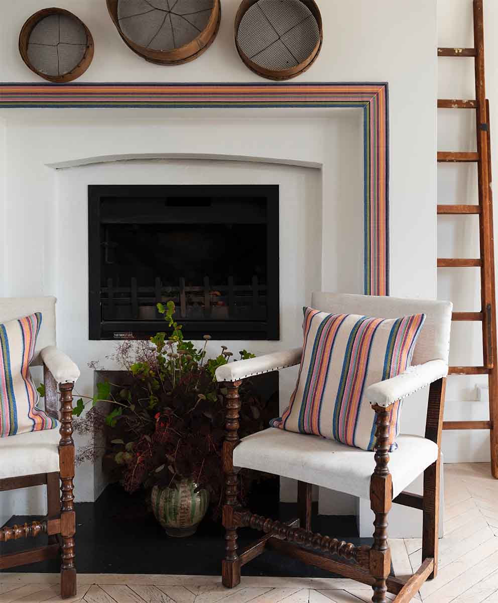 Image of Molly Mahon cushions made from the Odisha fabric with the cream base placed on chairs in front of a fireplace which is framed by Molly Mahons Odisha trim.