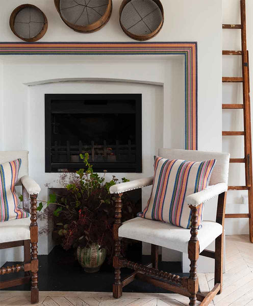Image of Molly Mahon cushions made from the Odisha fabric with the cream base placed on chairs in front of a fireplace which is framed by Molly Mahons Odisha trim.