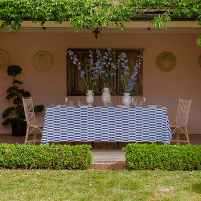 Outdoor dining setup with a tablecloth, chairs, and decorative elements in a garden setting.
