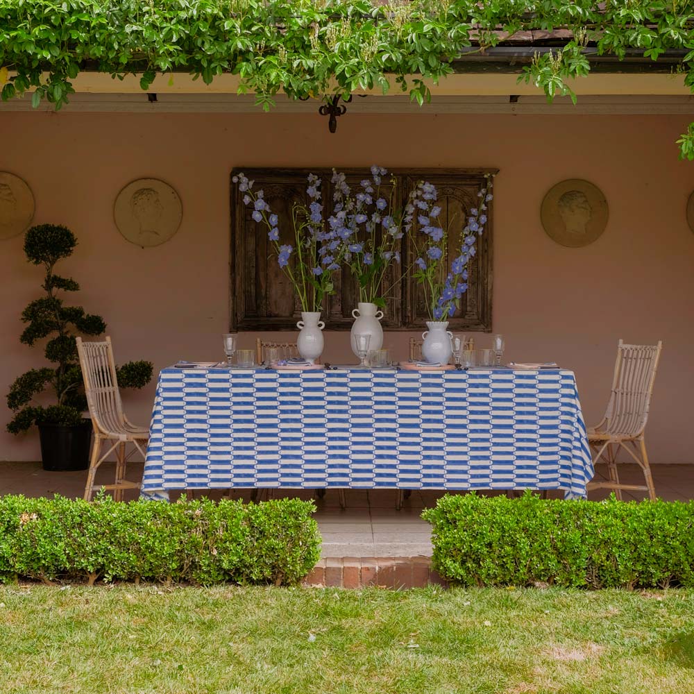 Outdoor dining setup with a tablecloth, chairs, and decorative elements in a garden setting.