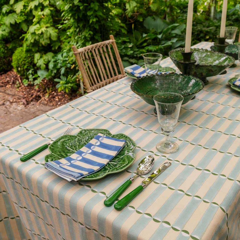 Dining table set with green plates, luna striped tablecloth, and outdoor setting