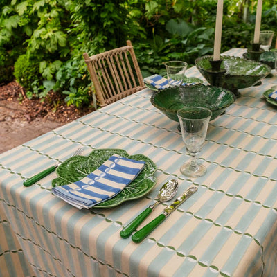 Dining table set with green plates, luna striped tablecloth, and outdoor setting