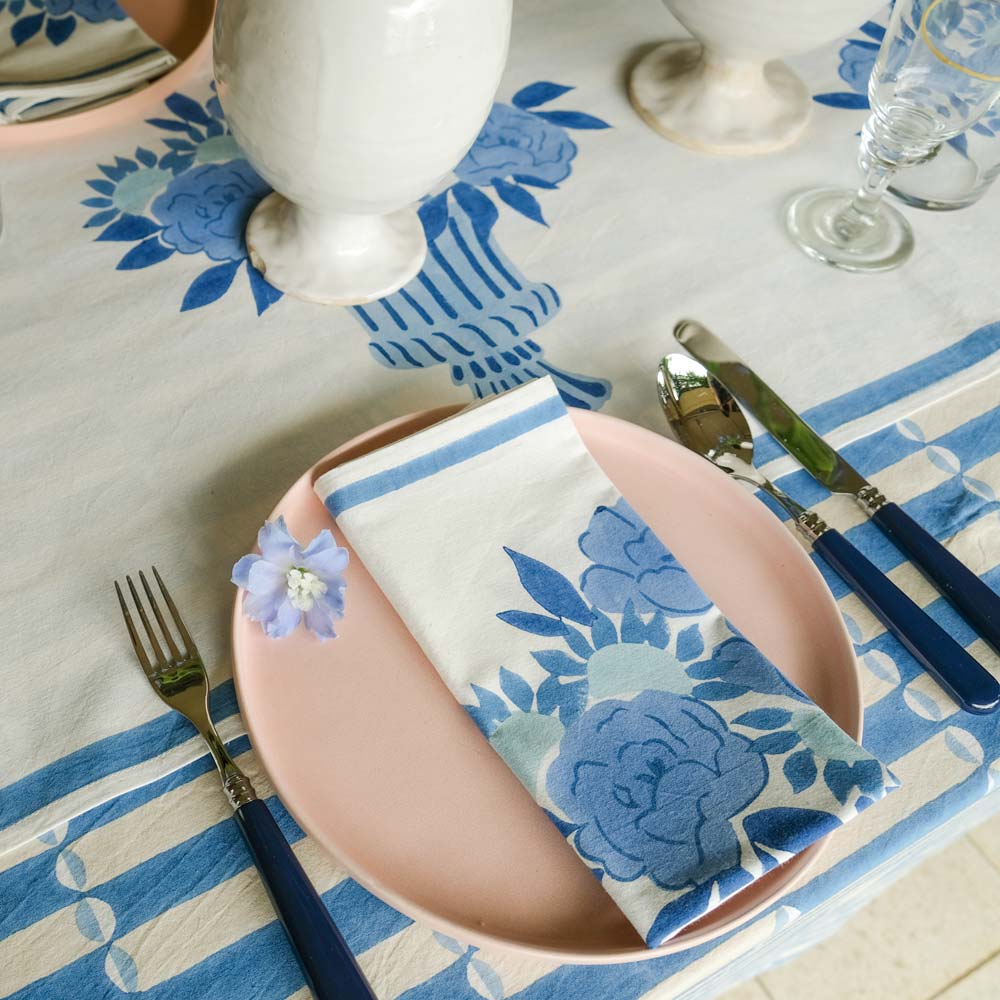 Dinner setting with floral tablecloth, plates, cutlery, and napkin on a table.