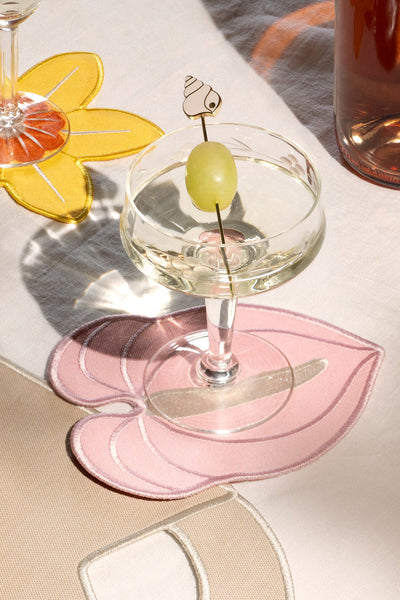 A coupe glass with a grape sits on Octaevo Pink Anthurium Coasters, atop a table with colorful placemats.