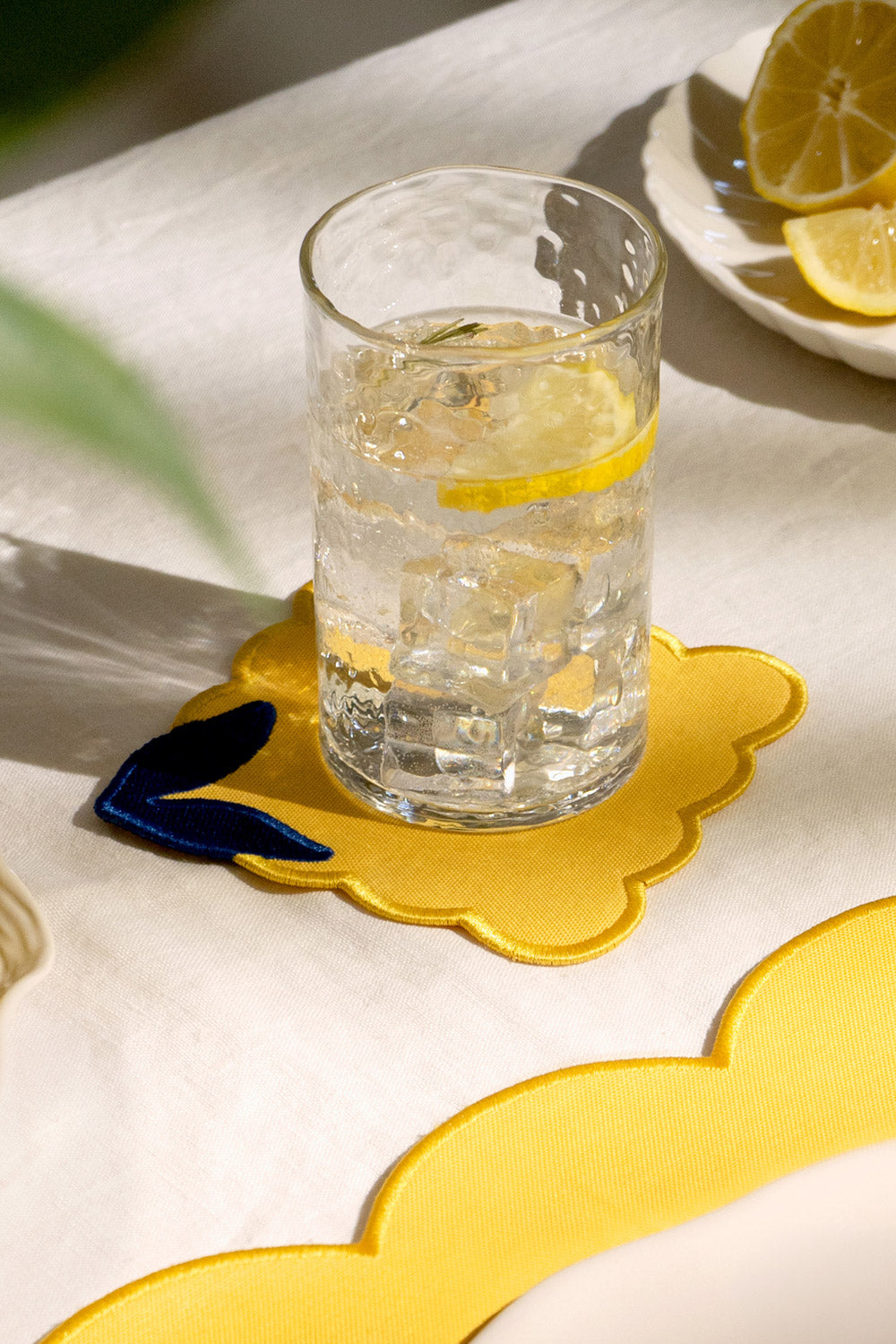 A glass of lemon water sits on an Octaevo Lemon Coaster (Set of 4), placed atop a white tablecloth.