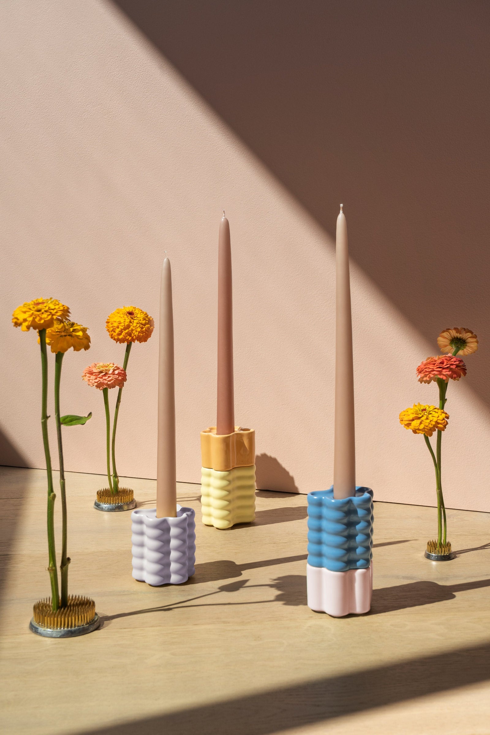 Three Octaevo Flora Candle Holders in orange with tall candles are arranged among flowers.