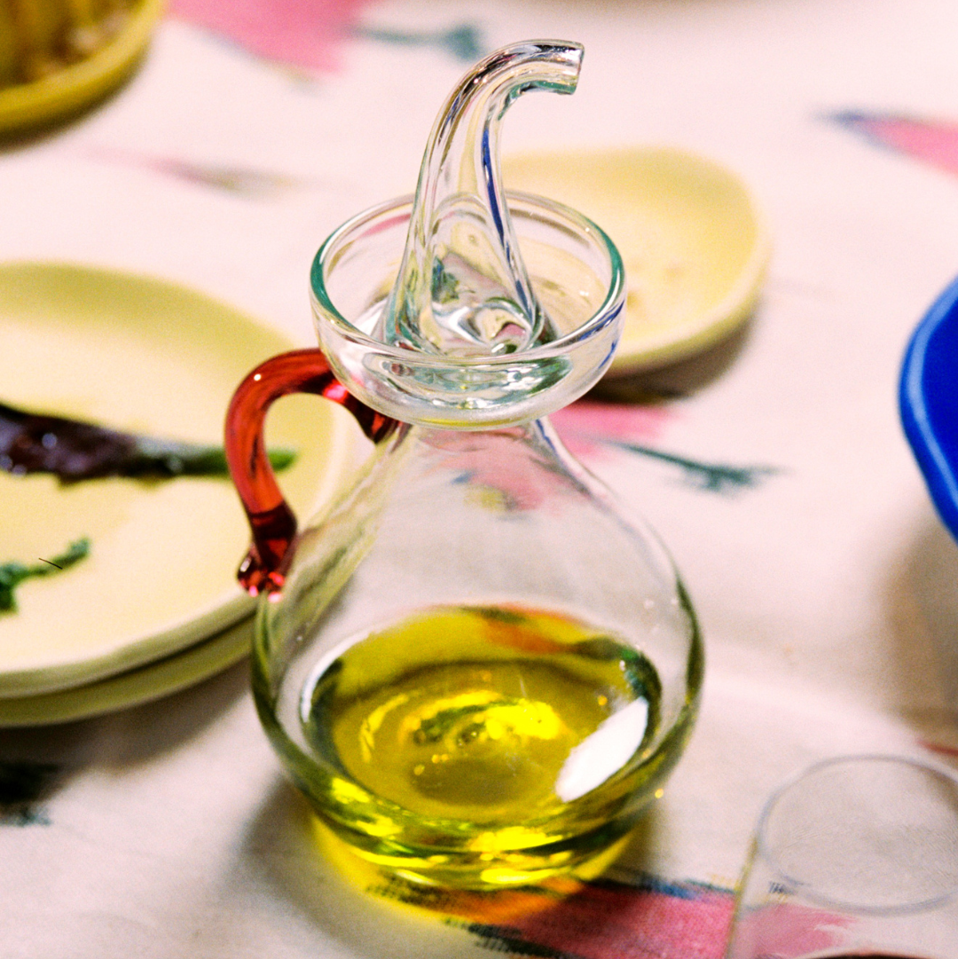  Olive cruet with olive oil on a table with plates in the background - lifestyle